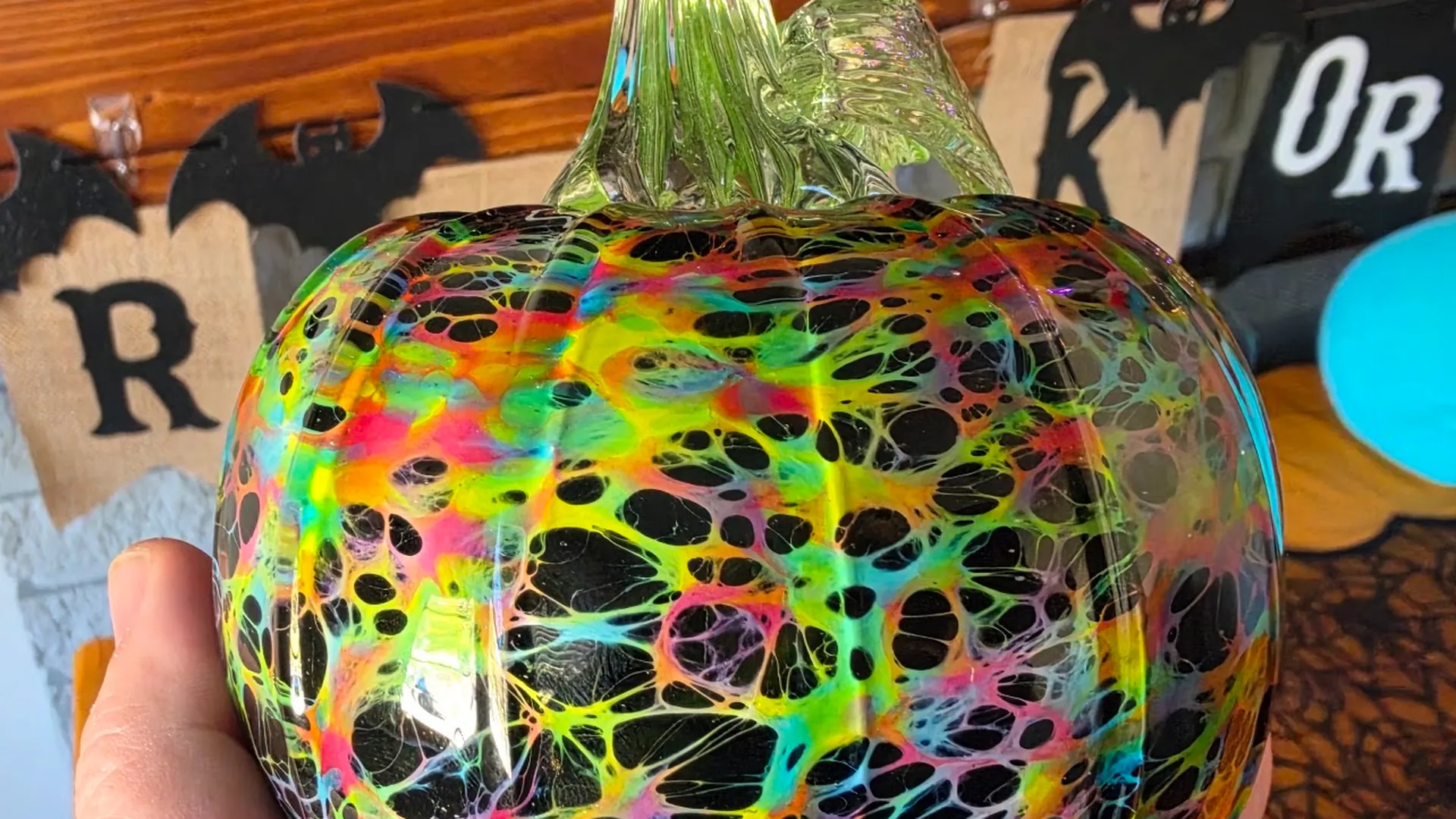 A hand-blown glass pumpkin with a neon web pattern over black, from Laura's collection