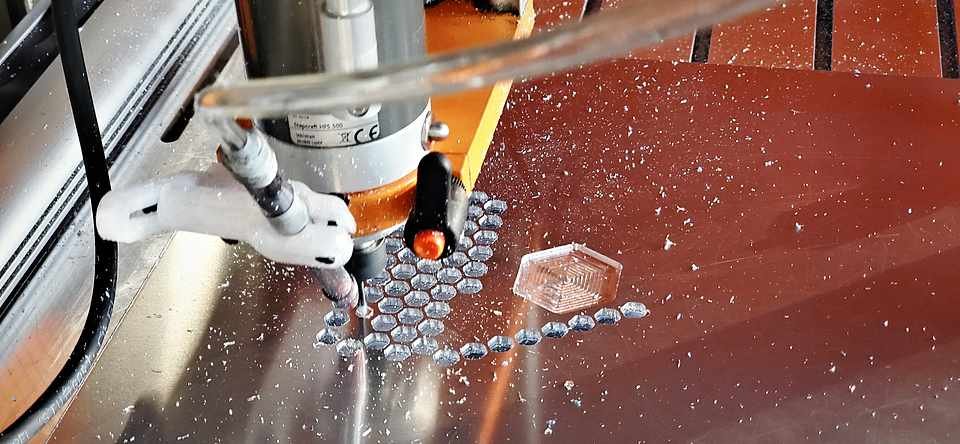 CNC router spindle cutting a pattern into aluminum sheet stock, chips scattered across the bed.