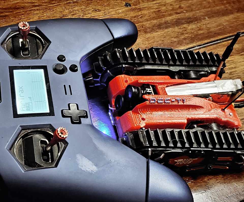 Custom FPV flight controller transmitter with an OLED telemetry screen, sitting on a wood workbench.