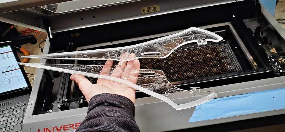 Hand lifting a freshly laser-cut clear acrylic part out of the Universal laser cutter's bed.
