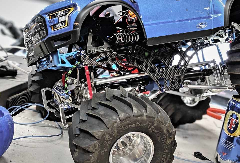 RC Ford Raptor monster truck mid-rebuild, carbon fiber chassis plates exposed under the rear bed and tires stacked beside it.