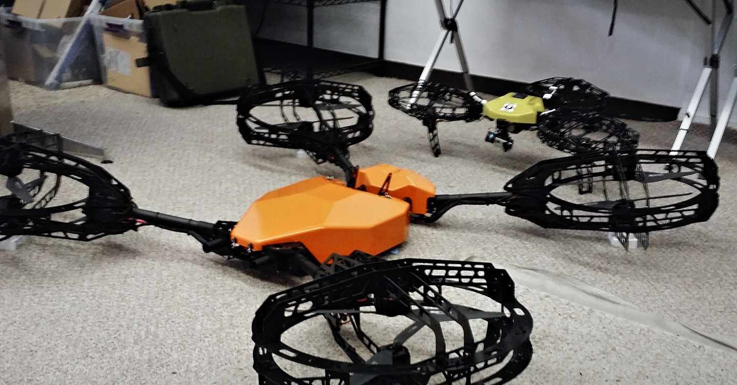 Full view of the orange quad-ducted hovering platform on the shop floor, four propeller shrouds and the central flight-control pod.