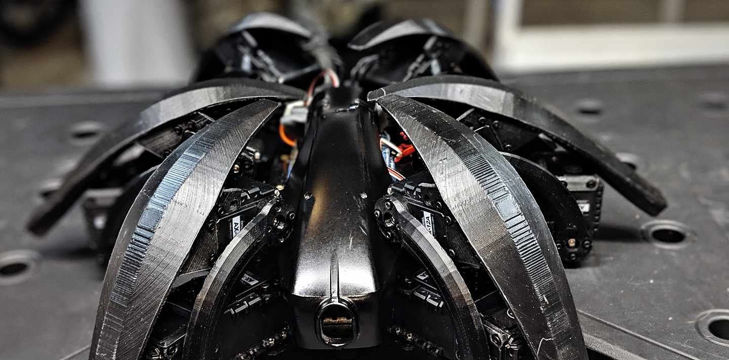 Head-on view of the hexapod robot, its printed leg shrouds fanned out like blades in low, dramatic light.