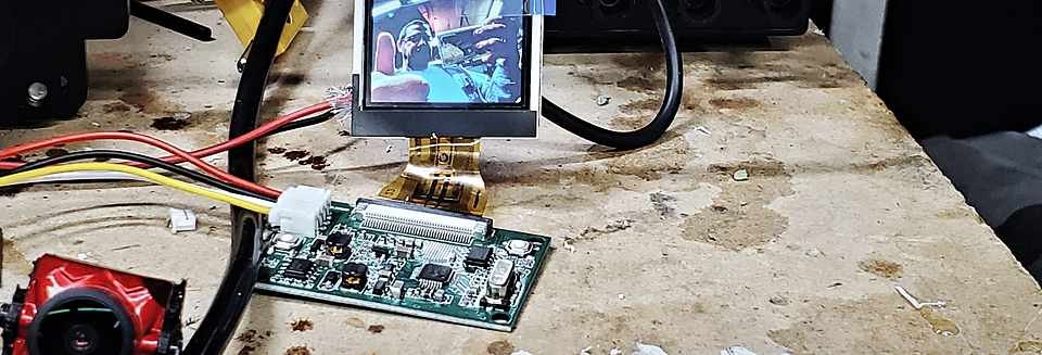 Flight controller dev board wired to an FPV camera module on the workbench, breadboard and wire spool behind it.