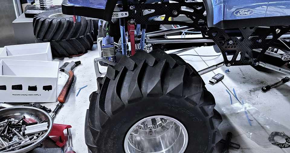 RC Raptor rear suspension and carbon fiber chassis rails, mid-rebuild under garage light.